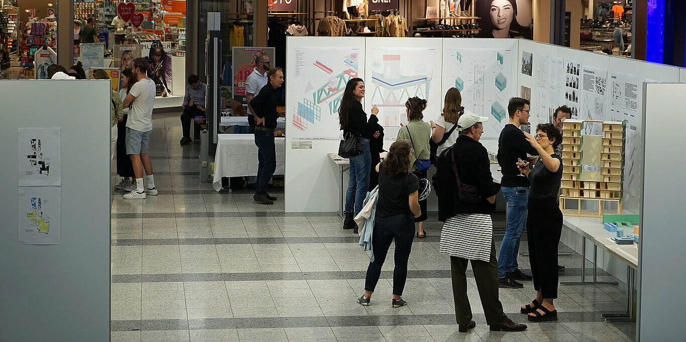 Mehrere Personen schauen sich eine Ausstellung von Plänen auf Stellwänden an.